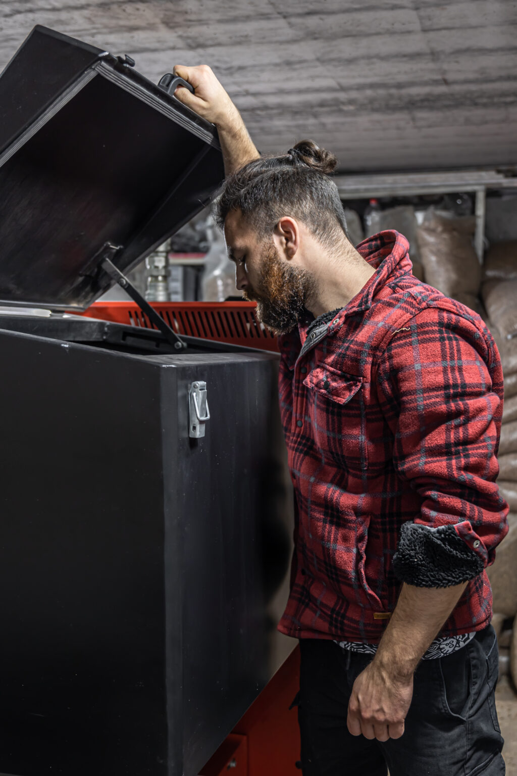 The young man looking into a solid fuel boiler, working with biofuels, economical heating.